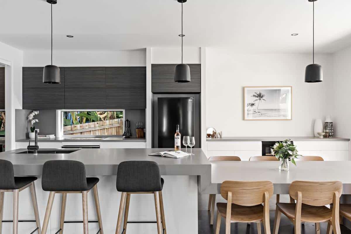 A modern kitchen with a central island, bar stools, and a dining area with wooden chairs.