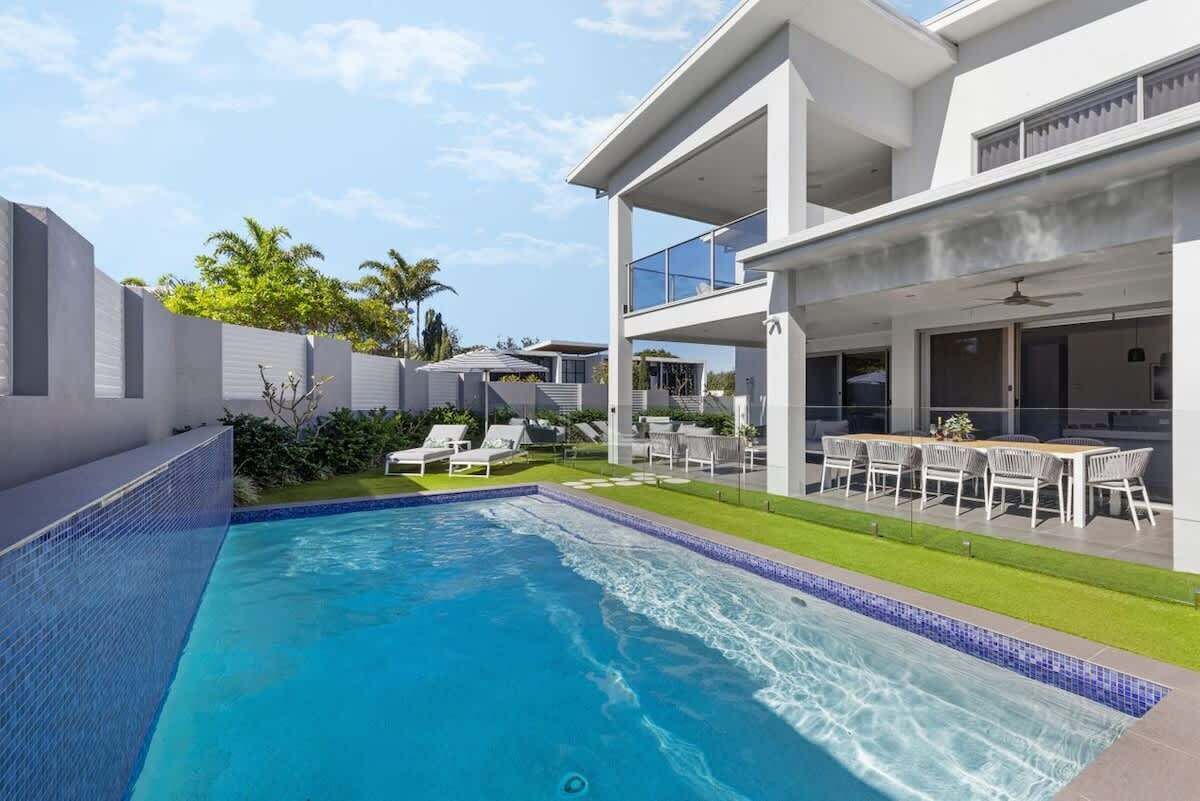 A modern two-story house with a swimming pool, outdoor seating, and a well-maintained lawn.