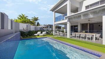 A modern two-story house with a swimming pool, outdoor seating, and a well-maintained lawn.
