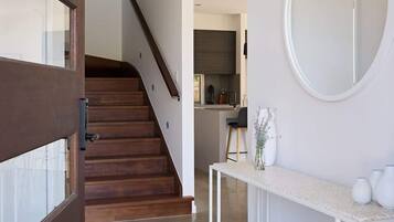 A modern interior with a wooden staircase, a kitchen area, and a white console table with a mirror.