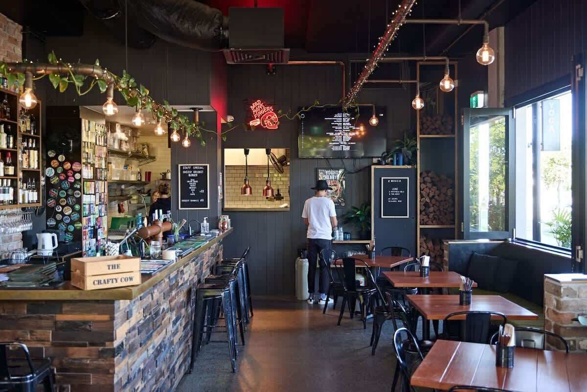 A restaurant interior with a bar area, seating, and a person working at the bar.
