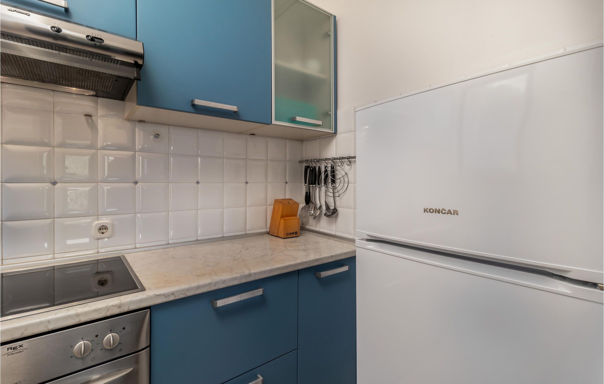 Une cuisine avec un réfrigérateur blanc, des armoires bleues, une cuisinière en acier inoxydable et un dosseret carrelé.