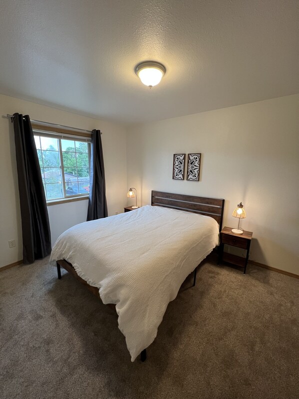 Quarto com cama, duas luminárias de cabeceira, janela com cortinas e dois objetos decorativos fixados na parede.