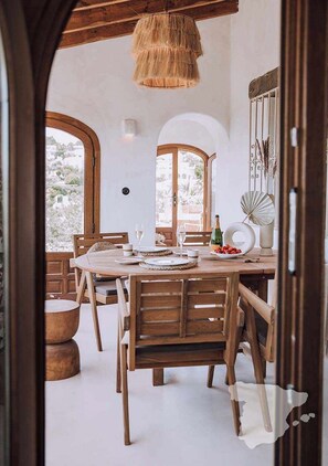Un espace repas avec des meubles en bois, un luminaire suspendu et une vue sur l’extérieur.