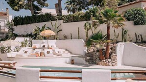 Un área de piscina con sillones blancos y una palmera.