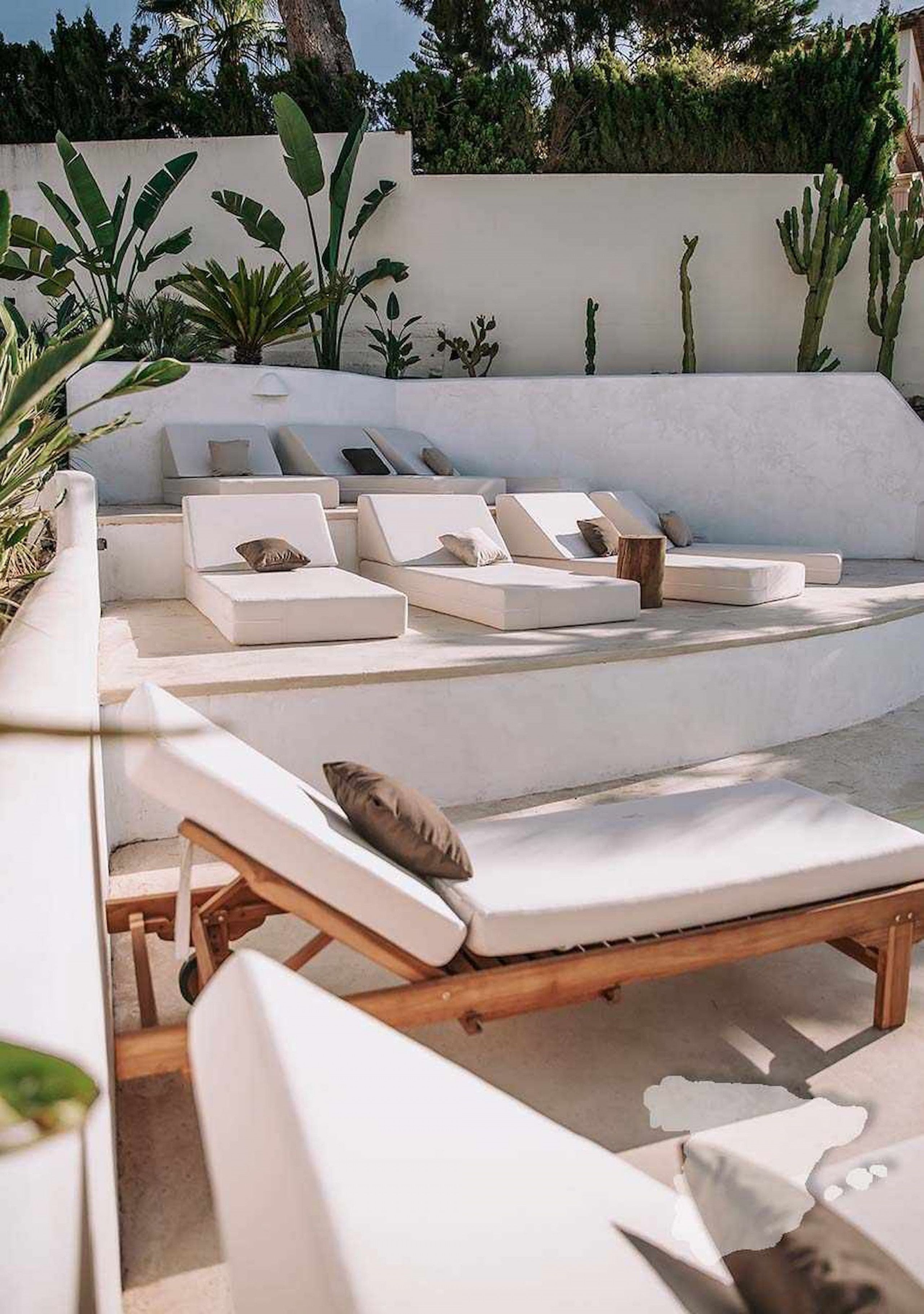 Een zonnig terras met witte, beklede zitplaatsen en een lage houten tafel.