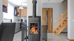 Una cocina moderna con estufa de leña, comedor con sofá negro y escalera de madera.