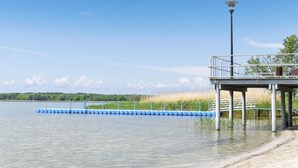 Un muelle se adentra en un lago tranquilo, con barandilla de metal y un farol.