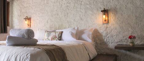 Quarto com cama, almofadas, manta e mesa de cabeceira com um vaso de flores.