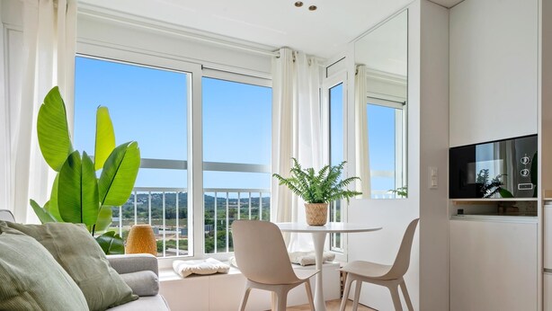 A modern living room with a sofa, two chairs, a small table, and a large window offering a view of the city. - Romantic loft sea views 8km from Port Aventura (La Pineda)