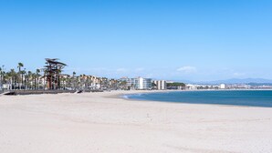 A beach with a palm tree-lined promenade, beachfront buildings, and a clear blue sky. - Romantic loft sea views 8km from Port Aventura (La Pineda)