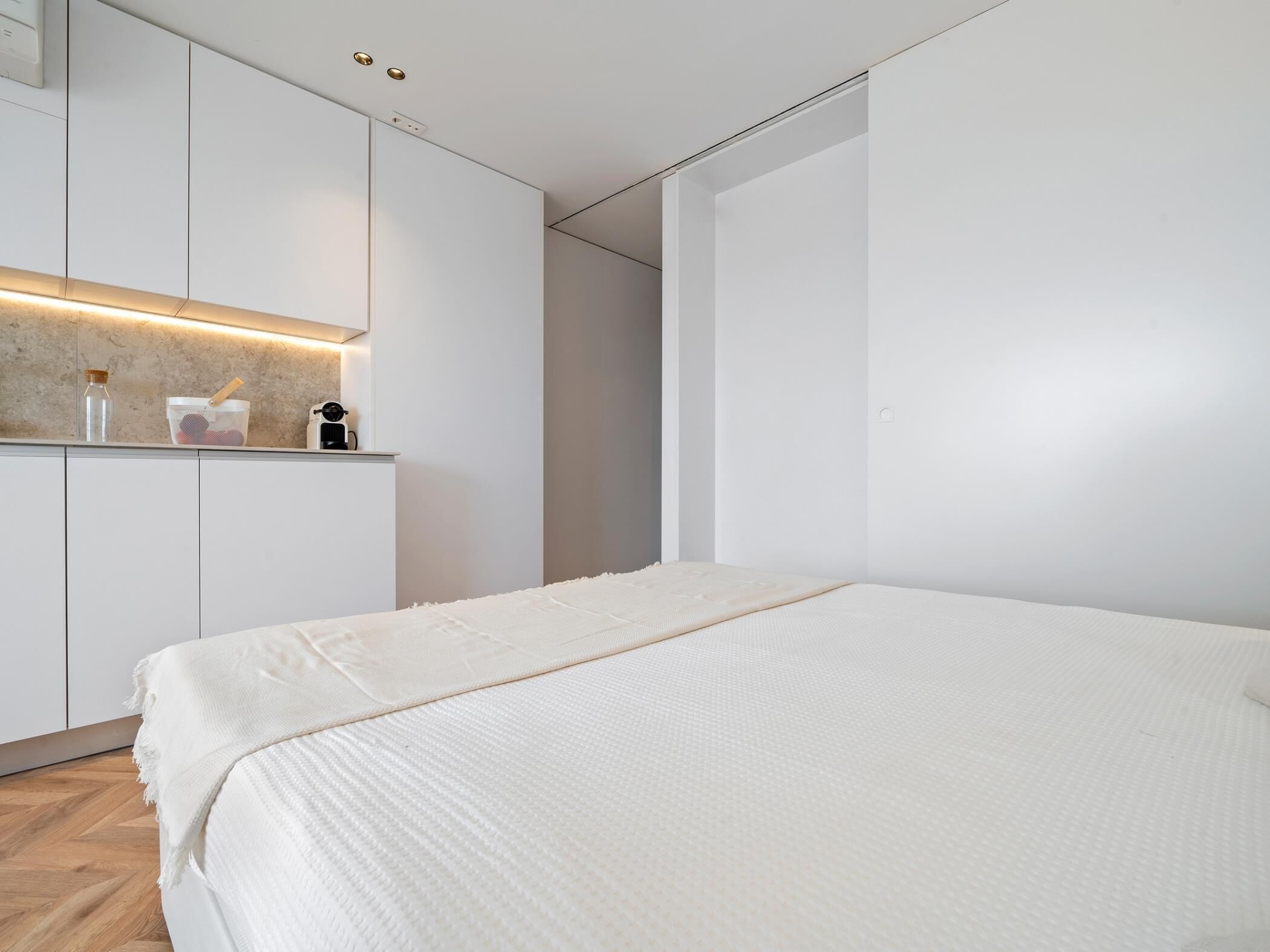 Un dormitorio moderno con una cama grande, un armario empotrado y una pequeña zona de kitchenette.