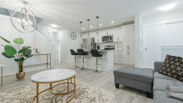 A modern kitchen with white cabinets, a central island with bar stools, and a chandelier.