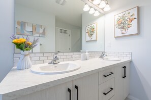 A modern bathroom with two sinks, a mirror, and a vase of flowers.