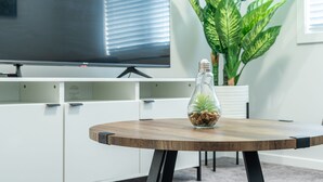 A modern room with a round wooden table, a TV mounted on the wall, and a large green plant.