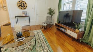Een woonkamer met een flatscreen televisie, een salontafel, een bank, een klein bijzettafeltje en een decoratieve wandversiering.
