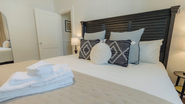 Een net opgemaakt bed met een gestoffeerd hoofdeinde, een stapel witte handdoeken en een bedlampje.