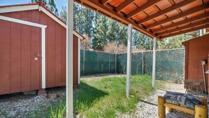 A covered outdoor area with a wooden bench, a red shed, and a green fence. - The Vintage Bear Cabin (Big Bear City)