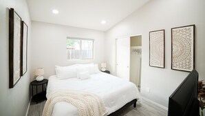 Quarto com cama, mesas de cabeceira, janela e arte nas paredes.