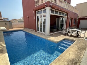 Una piscina con zona de patio, un área de estar cubierta y vistas a casas vecinas.