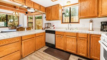 Une cuisine avec des meubles en bois, un lave-vaisselle, une cuisinière et une fenêtre donnant sur un paysage verdoyant.