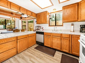 Une cuisine avec des meubles en bois, un lave-vaisselle, une cuisinière et une fenêtre donnant sur un paysage verdoyant.