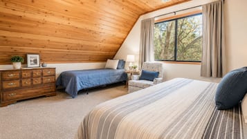 A bedroom with a sloped ceiling, two beds, a dresser, a chair, and a window with curtains.