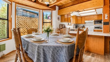 A dining area with a round table set for four, wooden chairs, a chandelier, and a view of the outside.