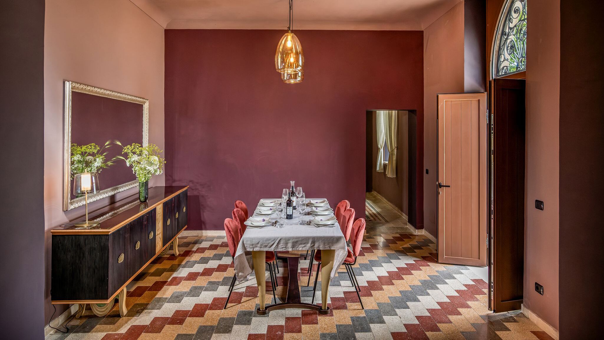 Een eethoek met een tafel voor vier personen, een spiegel en een decoratieve vaas met bloemen.