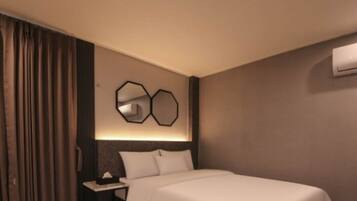 A hotel room with a bed, a desk, a chair, and a wall-mounted air conditioner.