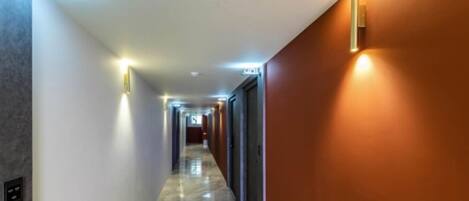 Un couloir d’hôtel avec un sol en marbre, un détecteur d’incendie et une porte sur la droite.