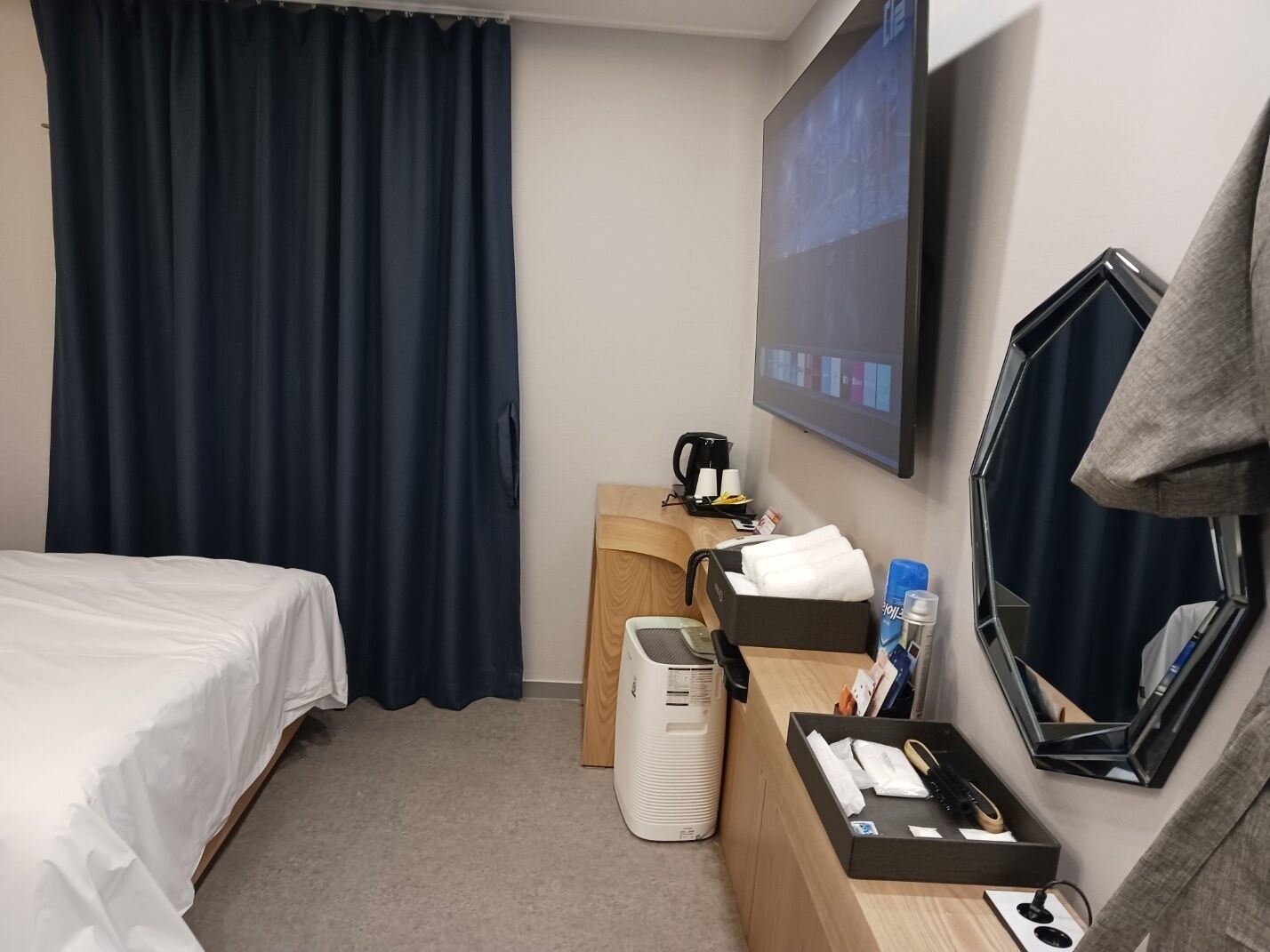A hotel room with a bed, a desk with a coffee maker, a mirror, and a TV on the wall.