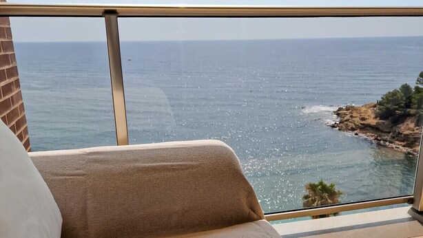 A balcony with a view of the sea, a book titled 'YOGA', and a pair of glasses on a cushion.