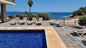 A pool area with lounge chairs and a view of the sea.