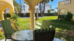 Une terrasse avec une table ronde et des chaises à rayures, entourée d’une arche jaune.