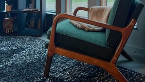 Ein Zimmer mit einem großen Fenster, einem grünen Sessel, einem Fernseher und einem Regal mit Gegenständen.