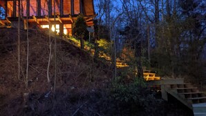 Una casa moderna con amplios ventanales y fachada de madera, rodeada de árboles y una escalera de piedra.