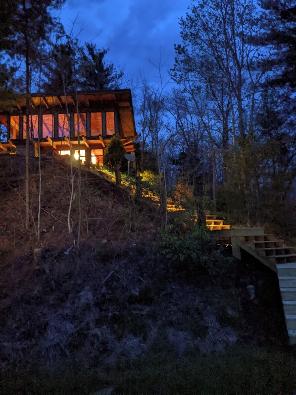 A modern house with large windows and a wooden exterior, surrounded by trees and a stone staircase.