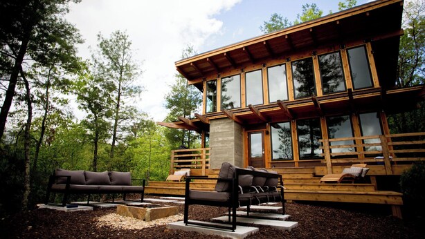 Una cabaña moderna de madera con ventanas amplias y mobiliario exterior.