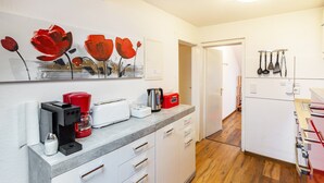 Een moderne keuken met een koffiezetapparaat, broodrooster en waterkoker op het aanrecht, een deur naar een andere kamer en een wandrek voor keukengerei.