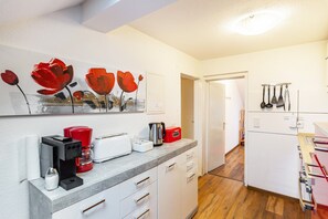 Una cocina moderna con cafetera, tostadora y hervidor sobre la encimera, una puerta que da a otra habitación y un soporte de utensilios en la pared.