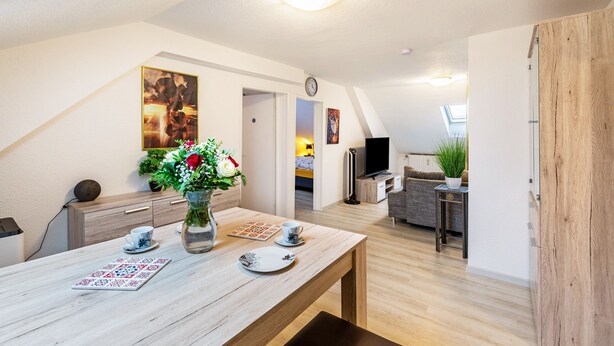 Een moderne woonkamer met een houten eettafel, een vaas met bloemen, een flatscreen televisie en een bank.