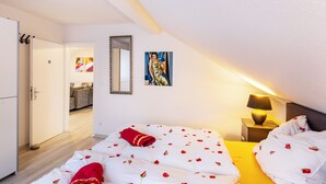 Een slaapkamer met een bed, nachtkastje, lamp, schilderij en een deur naar een andere kamer.