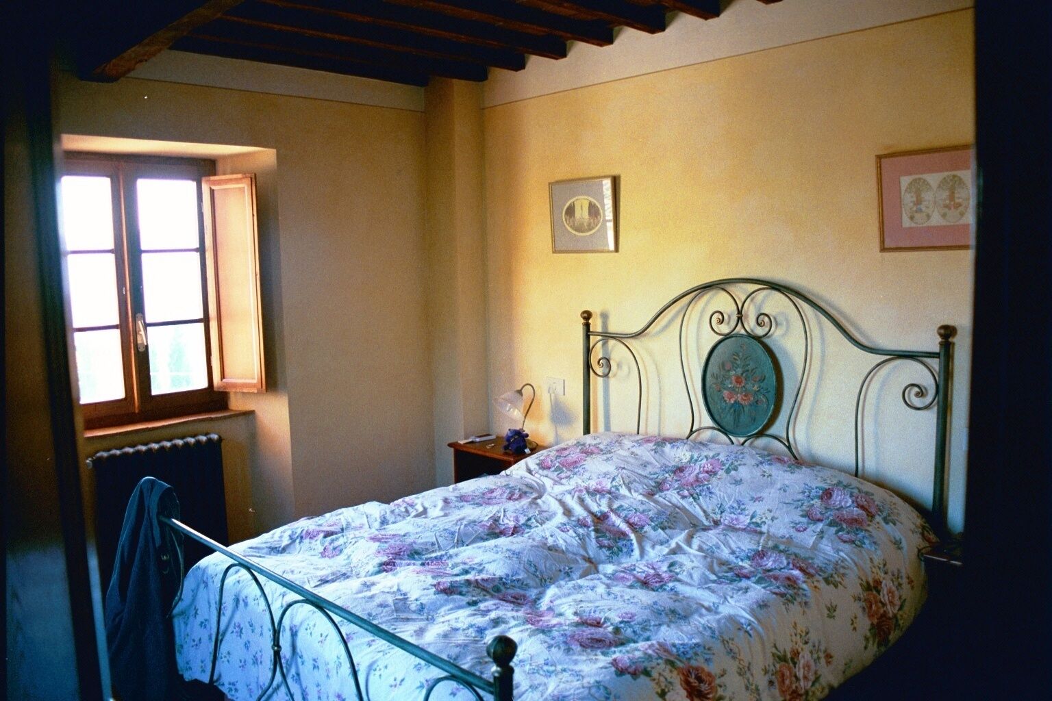 A bedroom with a bed, a nightstand, a window, and a radiator.