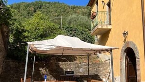 Eine Terrasss mit Tisch und Stühlen, einem weißen Sonnensegel und einer Steinmauer.
