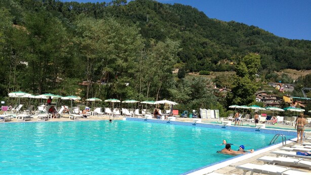 Ein Pool mit Liegestühlen und Sonnenschirmen, eingebettet in eine hügelige Landschaft.
