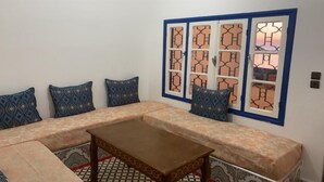 A living room with a sofa set, a coffee table, patterned cushions, and a decorative window with a geometric design. - Inviting 1-Bed Apartment in Ksar sghir (Ksar sghir)