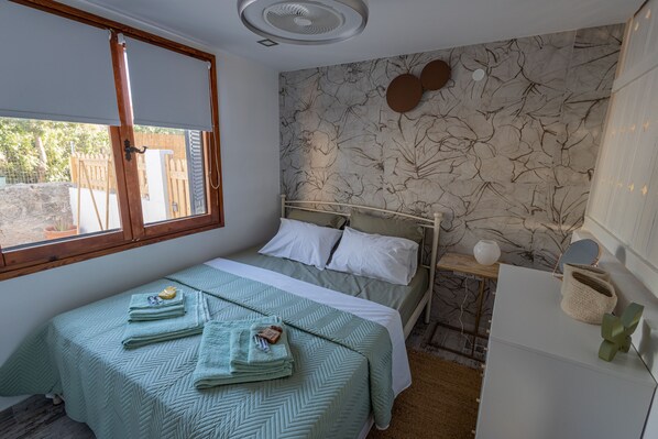 Une chambre à coucher avec un lit, une fenêtre, un mur orné d’un motif floral et un ventilateur de plafond.