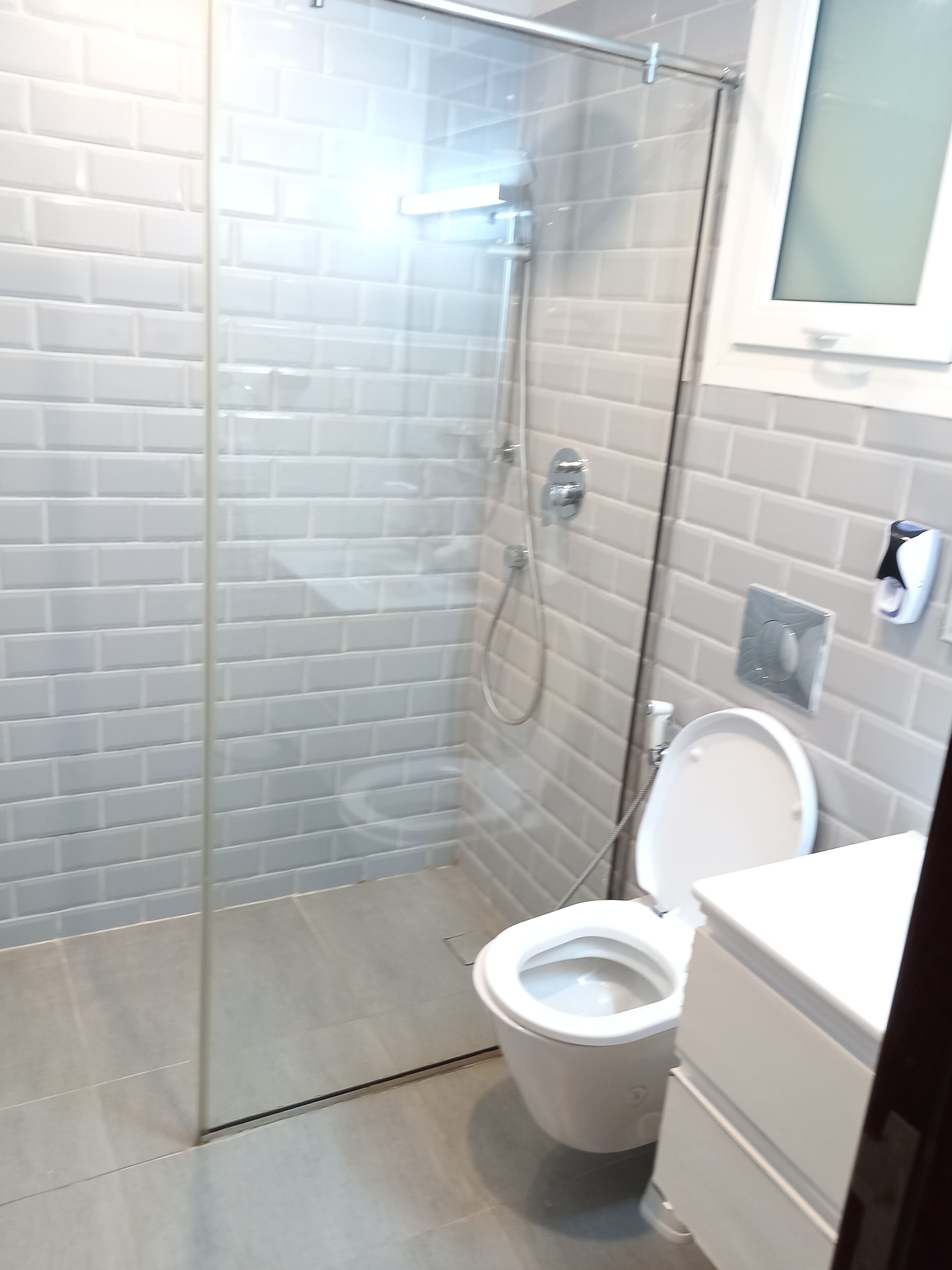 Un bany amb dutxa trencada amb portes de vidre, un vàter i un lavabo.