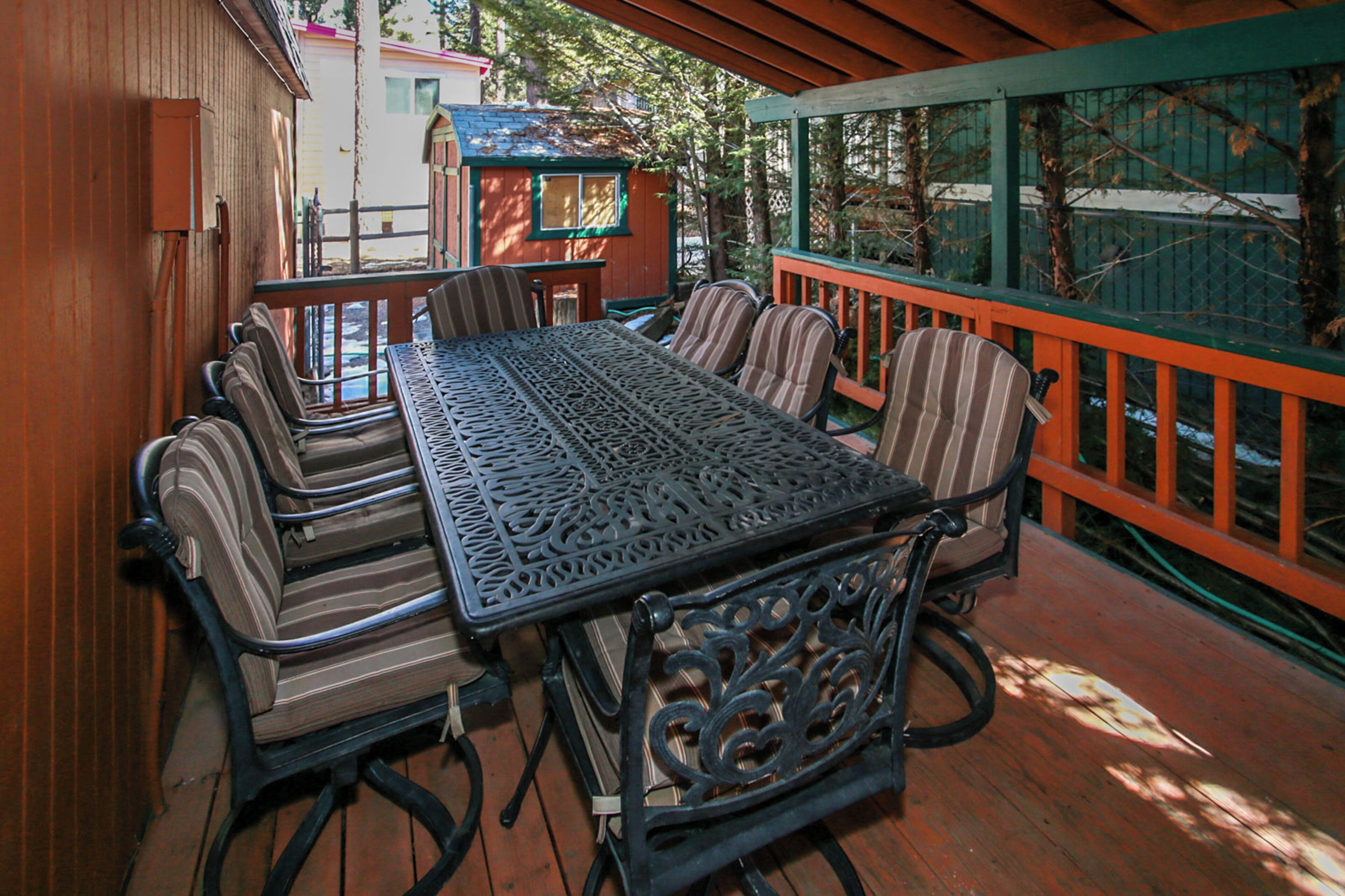 Eine überdachte Terrasse im Freien mit Tisch und Stühlen, umgeben von Holzgeländern und Bäumen.